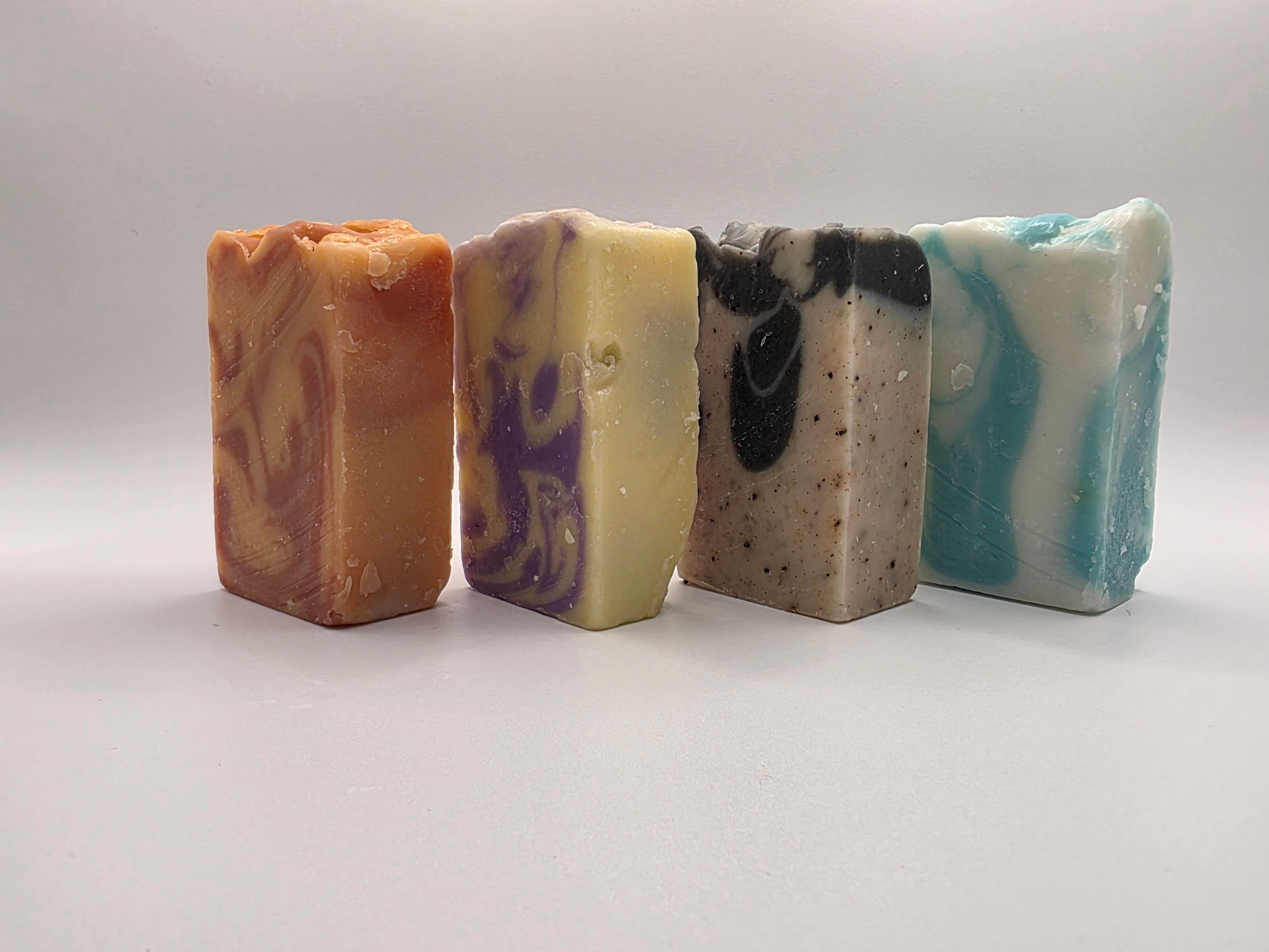 Four different colored soap bars on a light gray background